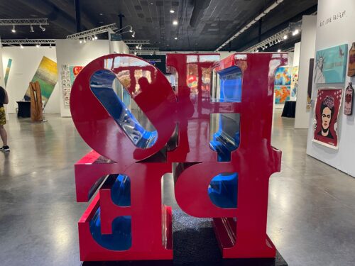 Red sculpture in center of room with with walls, more art