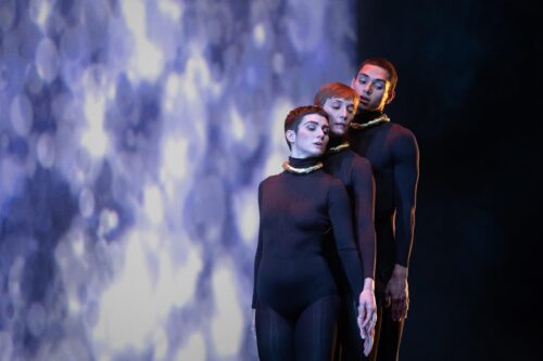 Three people standing together in a line, dressed in black.